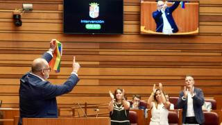 El procurador socialista Miguel Hernández Alcojor enarbola la bandera LGTBI en las Cortes durante la presentación de la proposición de Ley, en el pleno de este miércoles