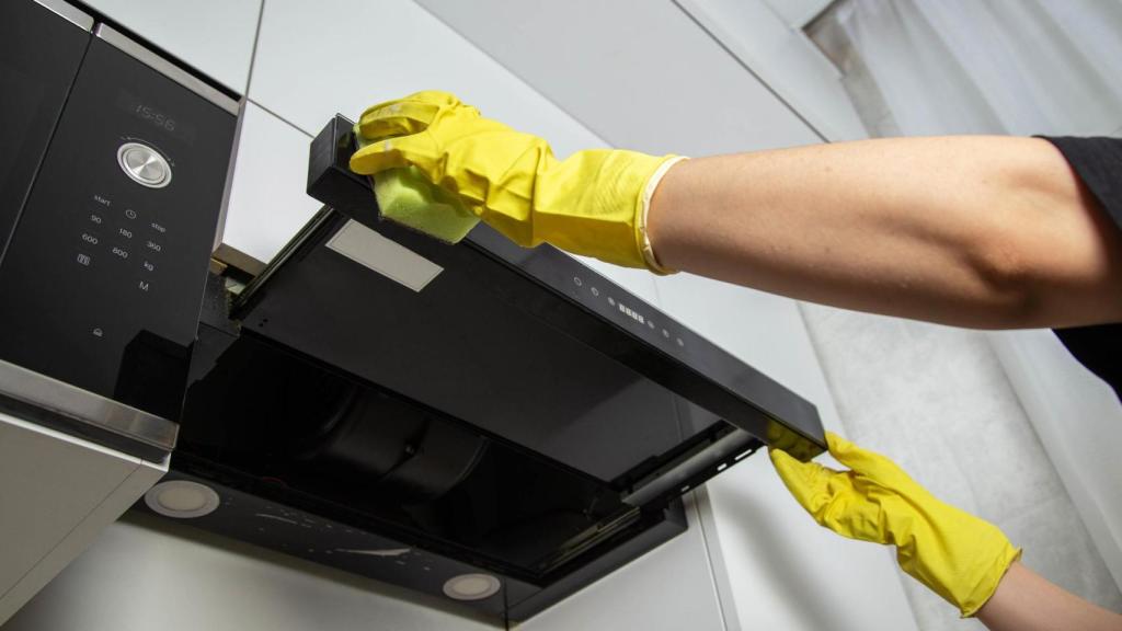 Manos con guantes limpiando la campana de cocina.