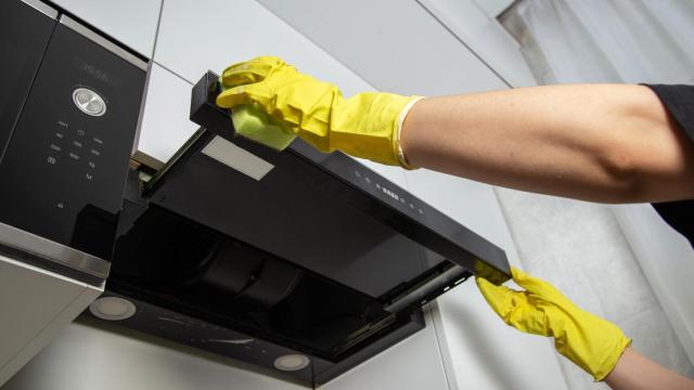 Manos con guantes limpiando la campana de cocina.