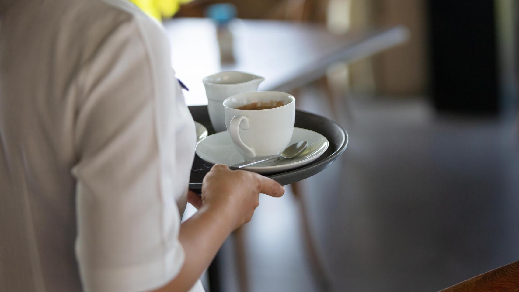 Un camarero lleva unos cafés a la mesa de unos clientes.