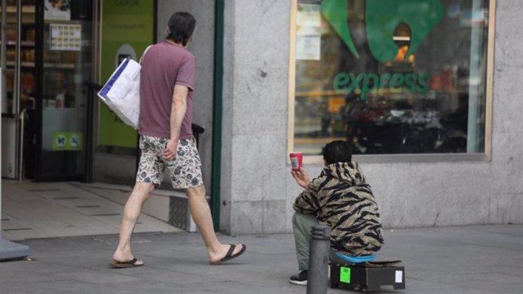 Una persona sin hogar pide dinero frente a un supermercado.