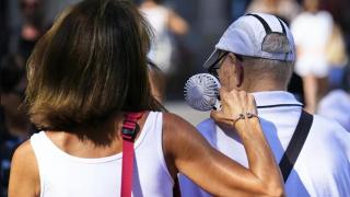 Una mujer apunta con un ventilador portátil a una persona mayor.