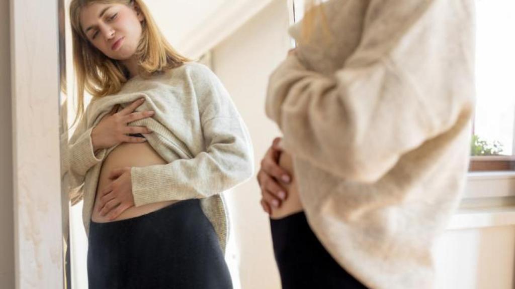 Mujer mirándose al espejo con el abdomen inflamado.