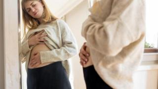 Mujer mirándose al espejo con el abdomen inflamado.