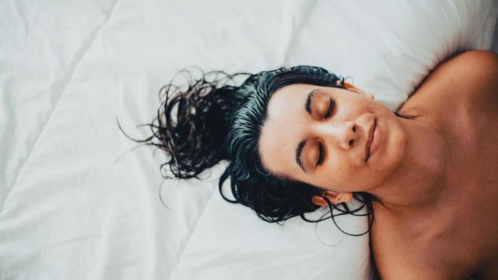 Mujer con el pelo mojado sobre la cama.