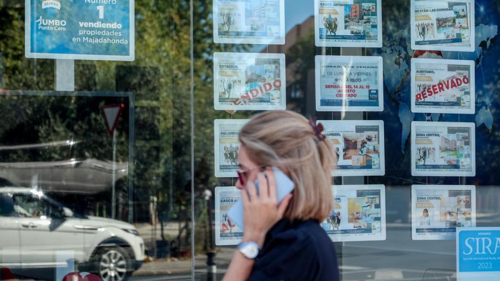 Una mujer camina frente a un escaparate de anuncios de viviendas
