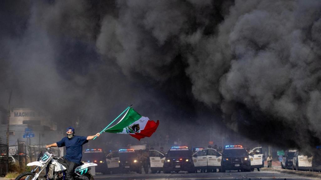 Un manifestante enarbola la bandera mexicana frente a una línea de policías durante las protestas contra las redadas del Servicio de Inmigración y Control de Aduanas (ICE) en Los Ángeles.