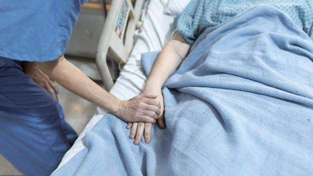 Una enfermera sostiene la mano de un paciente en cuidados paliativos.