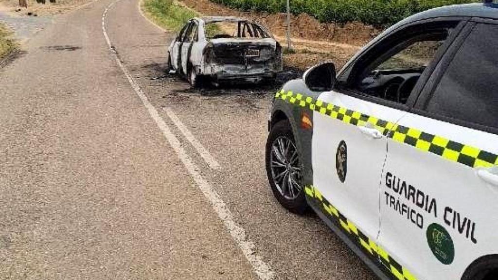 El vehículo calcinado y un coche de la Guardia Civil