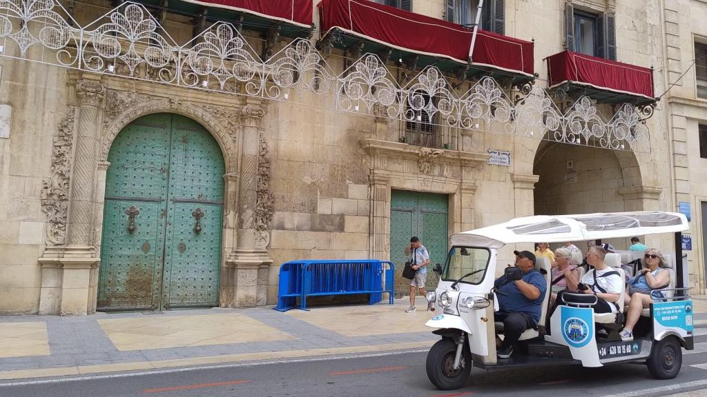 Un vehículo tipo tuc tuc pasa frente al Ayuntamiento de Alicante.