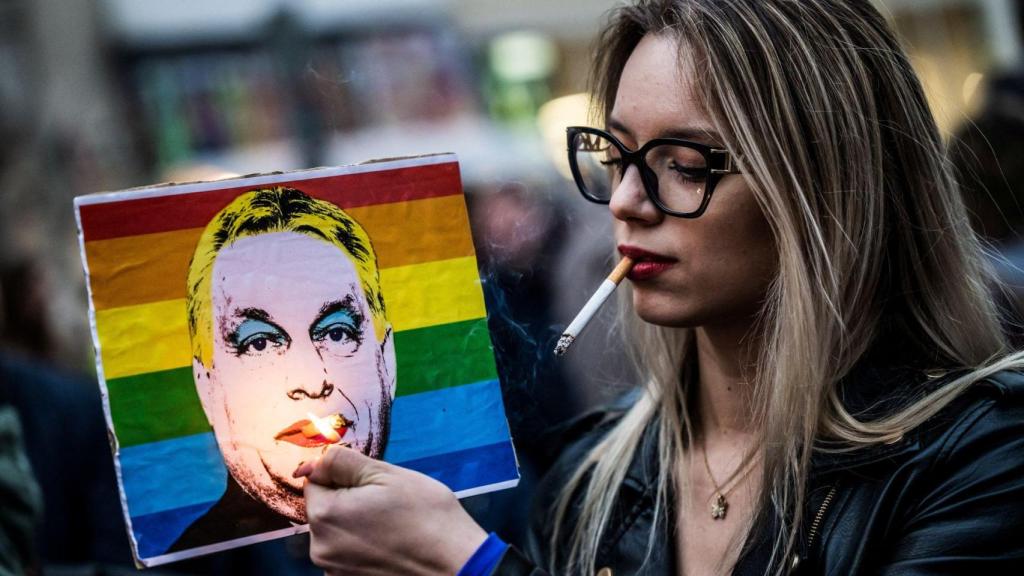 Una mujer enciende un cigarrillo colocado en una pancarta que representa al primer ministro húngaro, Viktor Orbán, durante una manifestación en Budapest.