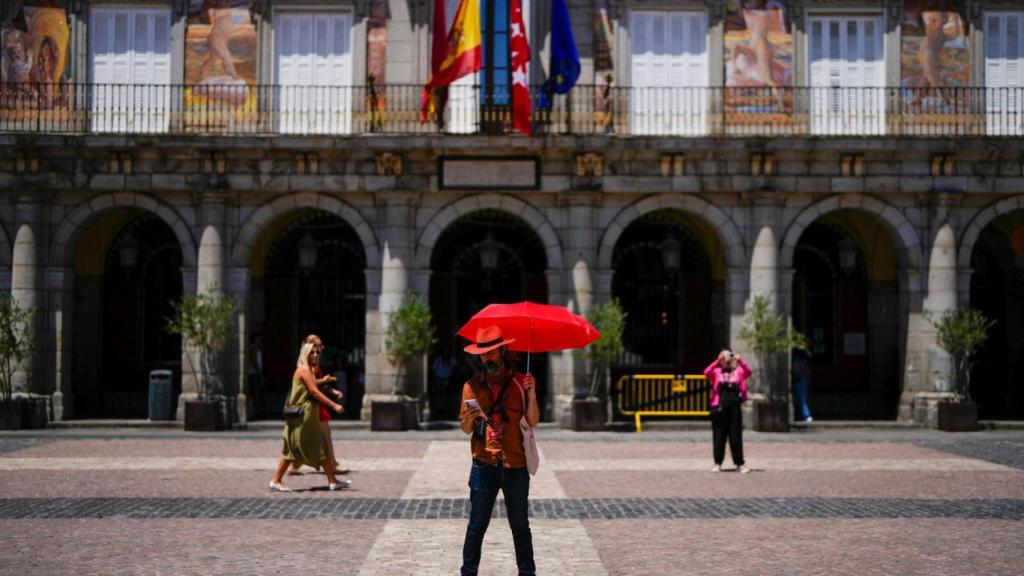 Un hombre se protege del sol con un paraguas en la Plaza Mayor de Madrid.