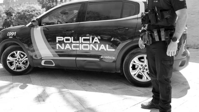 Un policía nacional, frente a su coche patrulla.