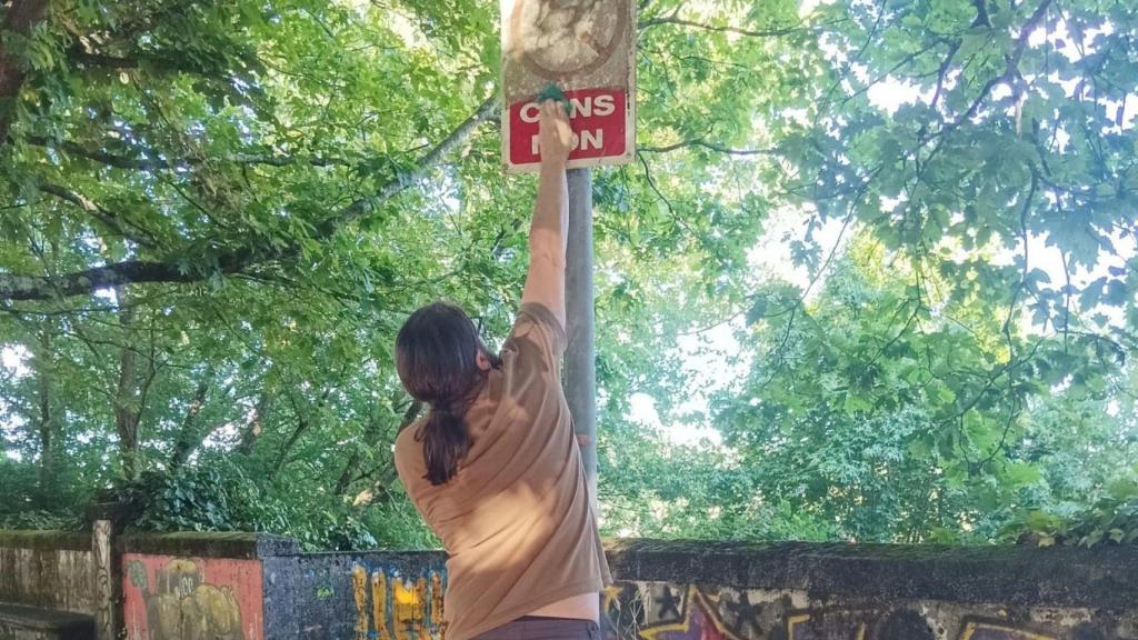 Un padre limpia un cartel en el parque infantil de A Trisca, en Santiago.