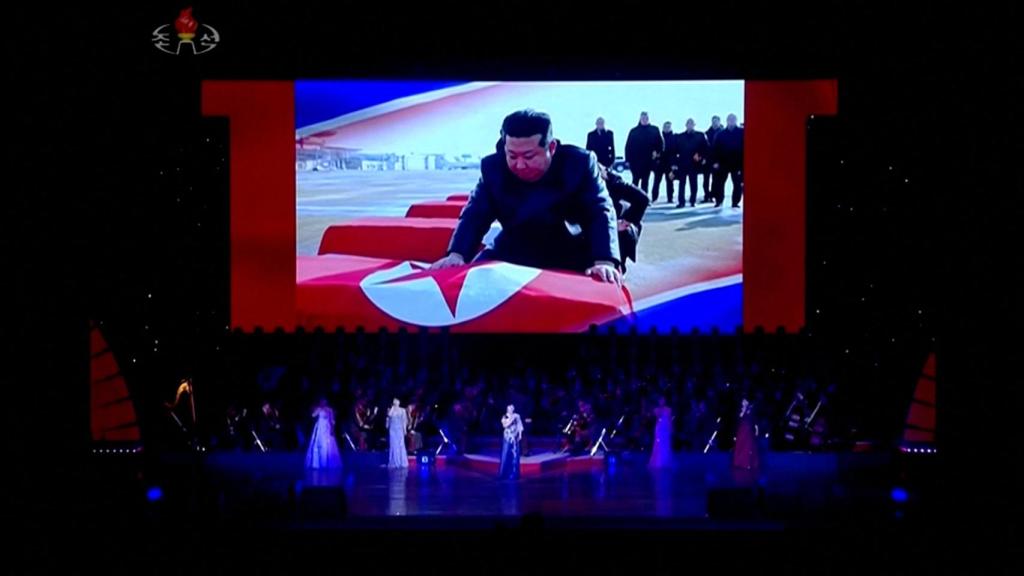 Artistas sobre el escenario mientras se proyecta en una pantalla la imagen de Kim Jong-un cubriendo ataúdes con la bandera norcoreana, en Pyongyang, Corea del Norte, el 29 de junio de 2025, en esta imagen tomada de un vídeo.