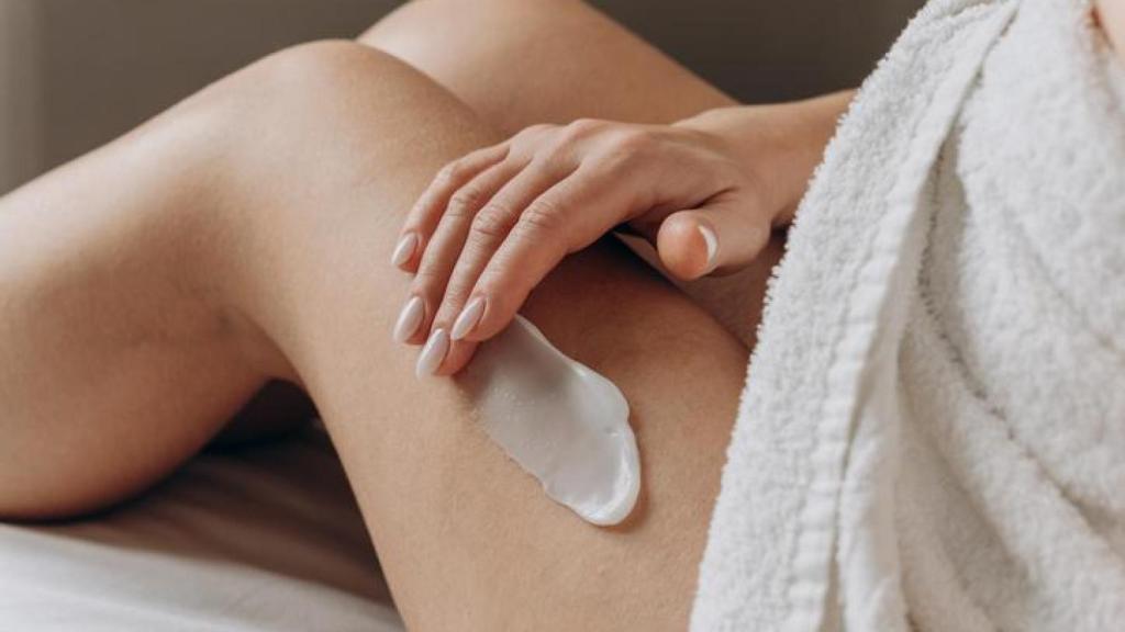 Mujer aplicándose crema en las piernas.