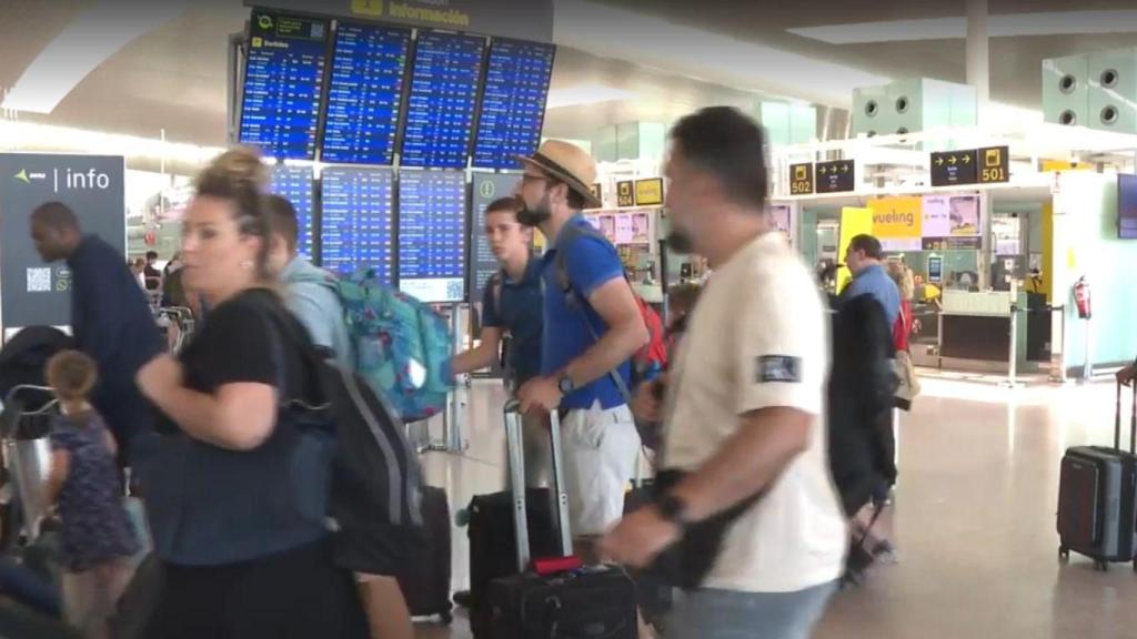 Un grupo de personas pasando por la pantalla de información en el aeropuerto de Barajas.