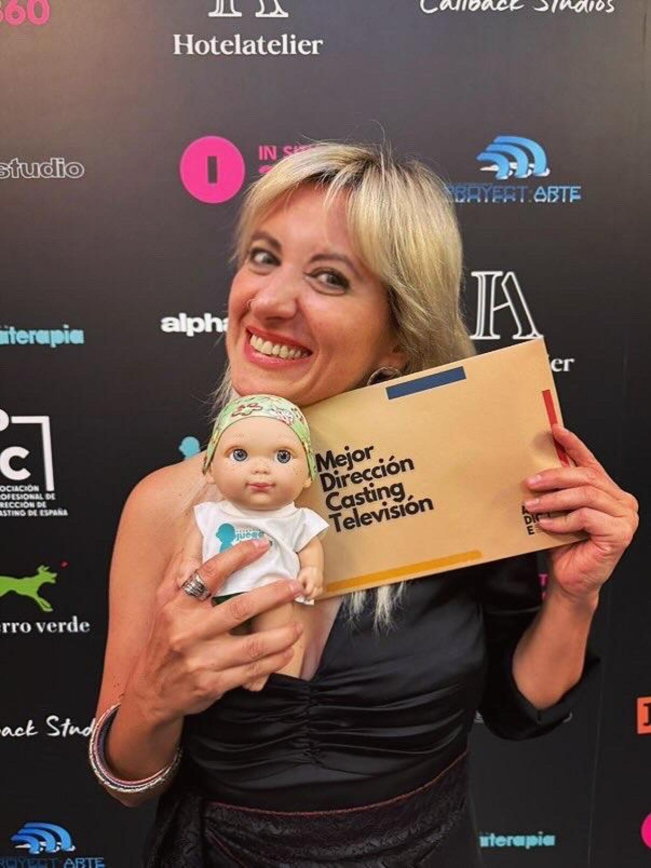 Reichel Delgado posa muy sonriente con la tarjeta de Mejor Dirección de Casting de Televisión y con el muñeco solidario Baby Pelón.