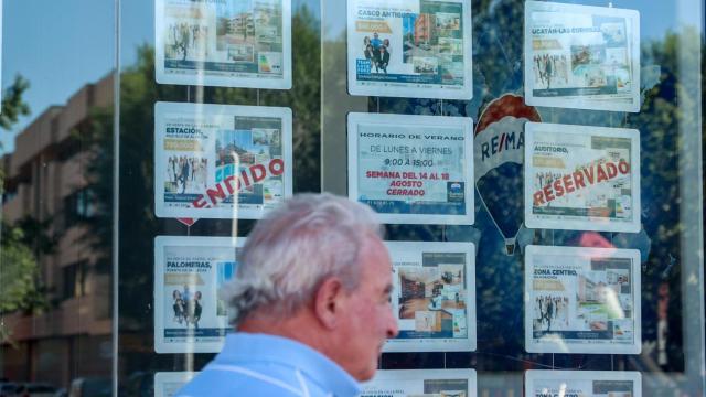 Un hombre camina frente a un escaparate de anuncios de viviendas