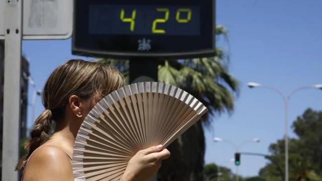 Una mujer se abanica mientras pasa por un termómetro de calle que marca 42 grados en Córdoba.