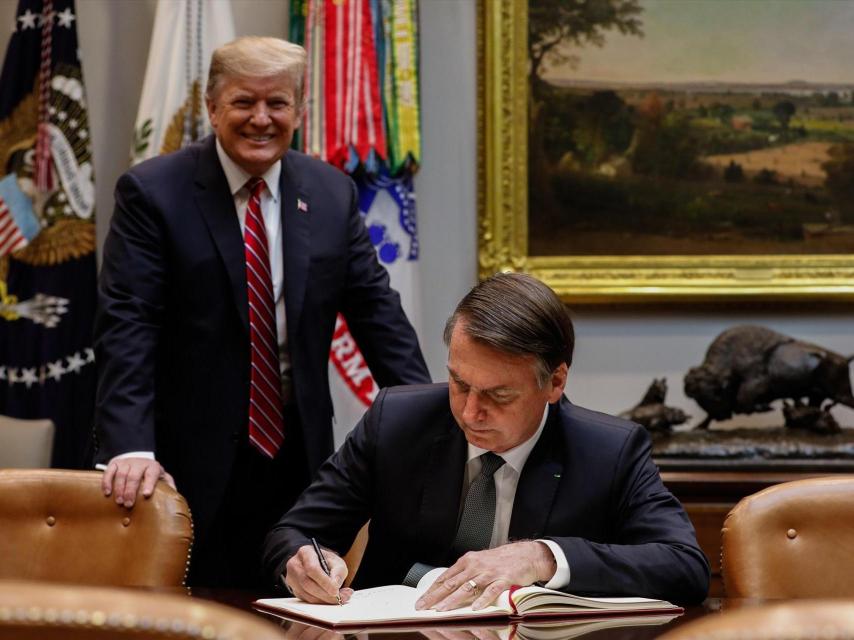 El presidente estadounidense Donald Trump junto al expresidente brasileño Jair Bolsonaro firma en el libro de visitas de la Casa Blanca