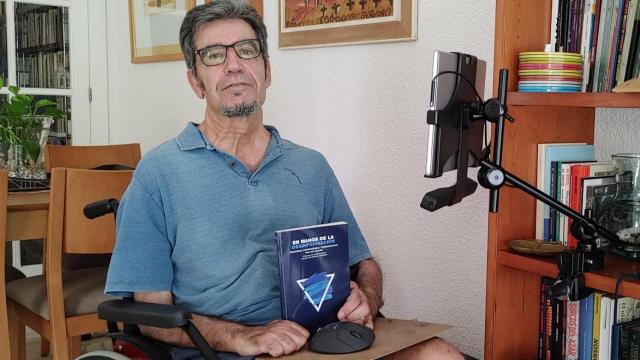 Pepe Reig, en su salón, frente a su ordenador, sujeta el último libro que ha escrito. EE