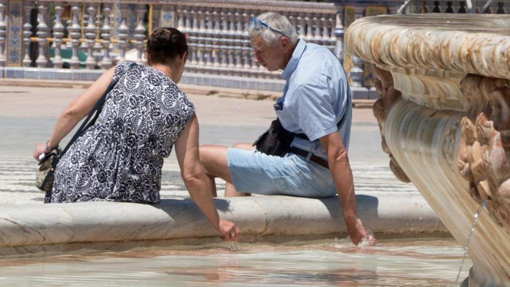 Dos turistas tratan de refrescarse en una fuente.