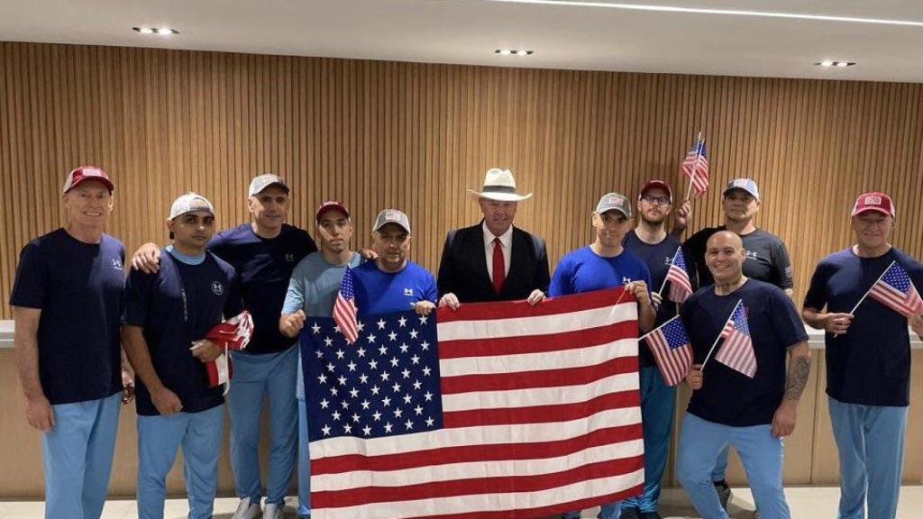 Dahud Hanid‑Ortiz, autor del triple asesinato de Usera, el segundo por la derecha y con una gorra, levanta una bandera de EEUU junto a otros nueve estadounidenses libertados por Venezuela.