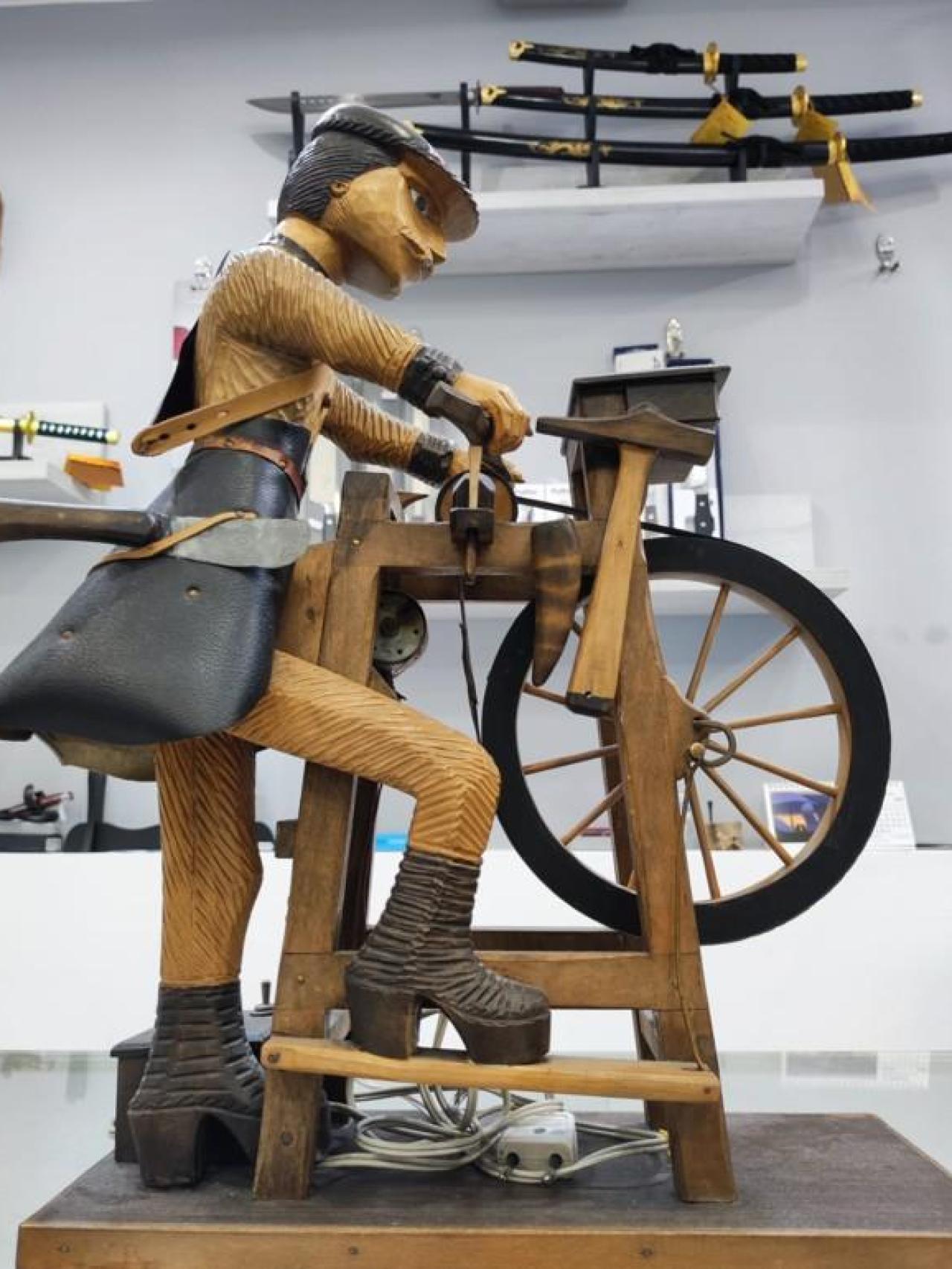 Pieza artesanal de un afilador, con sables en vainas detrás.