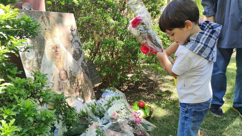 Un niño ofrece unas flores a una imagen de la Virgen del Prado.