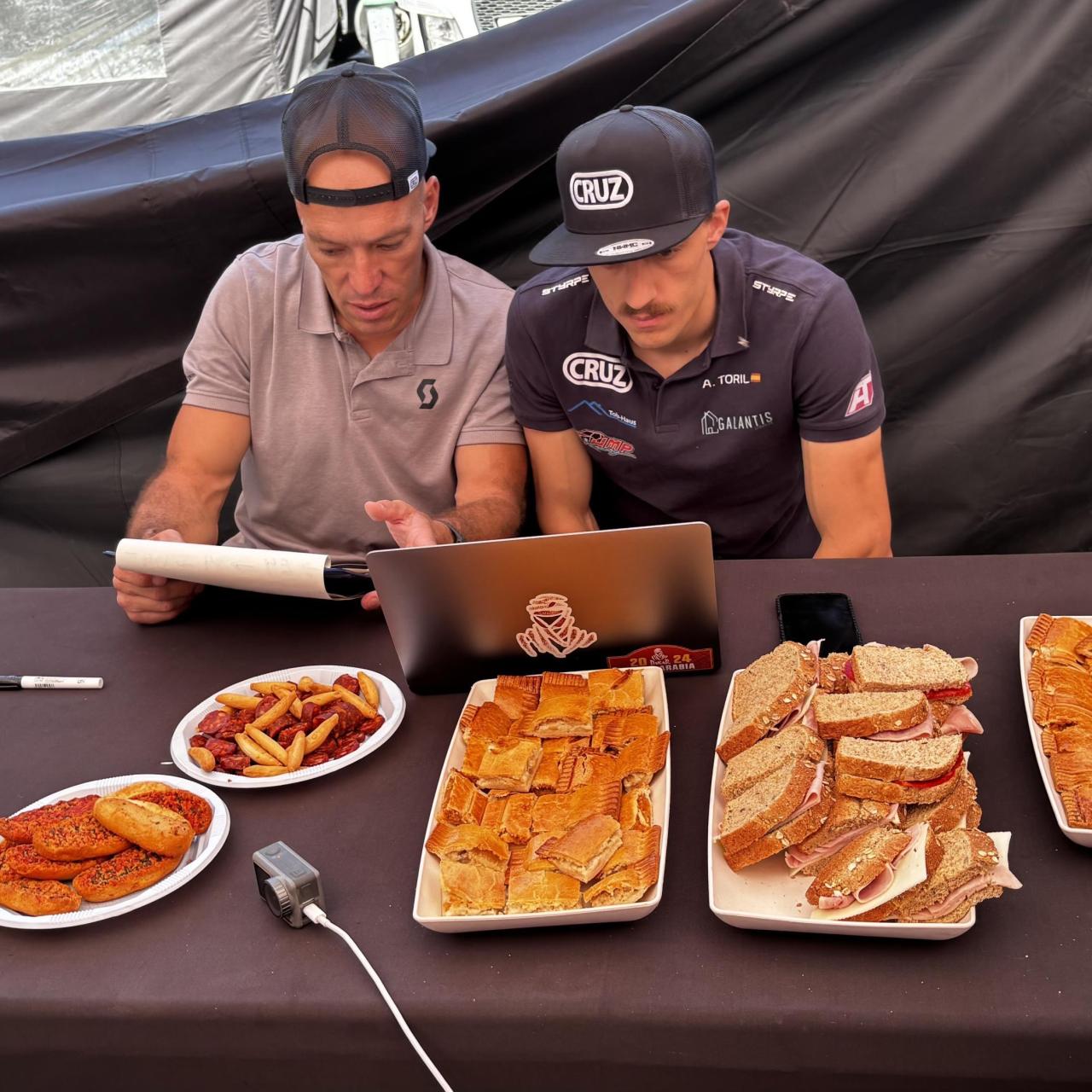 El copiloto Daniel Jordao (i) y el piloto Alex Toril (d) repasan el roadbook de la prólogo de la Baja Aragón 2025 mientras comen.