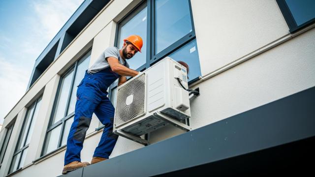 Imagen creada con IA de un trabajador colocando un aparato de aire acondicionado en una fachada.