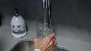 Una persona llena un vaso de agua de un grifo