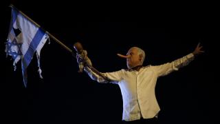 Un manifestante con una nariz postiza y una máscara del primer ministro israelí Benjamin Netanyahu sostiene un muñeco y una bandera israelí rasgada mientras participa en una protesta para exigir el fin de la guerra en Gaza.