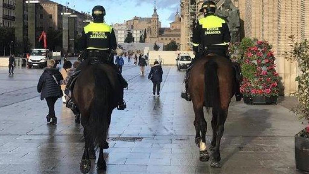 Dos agentes de la policía local montados sobre dos miembros del escuadrón, en la plaza del Pilar de Zaragoza.