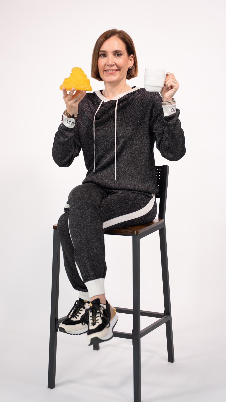 Boticaria García con una representación de la grasa corporal en una mano y un café en la otra.