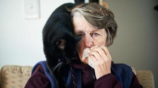 Una señora alergica a los felinos, con un gato en la espalda.