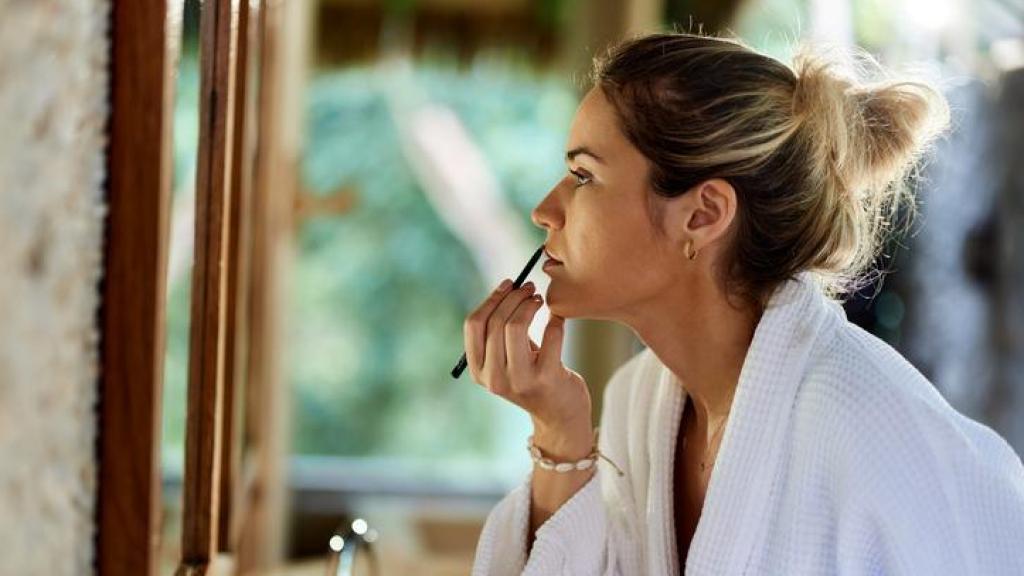 Mujer maquillándose los labios frente al espejo.