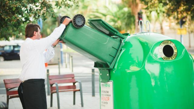 Un hostelero vaciando sus botellas de vidrio en el contenedor verde.