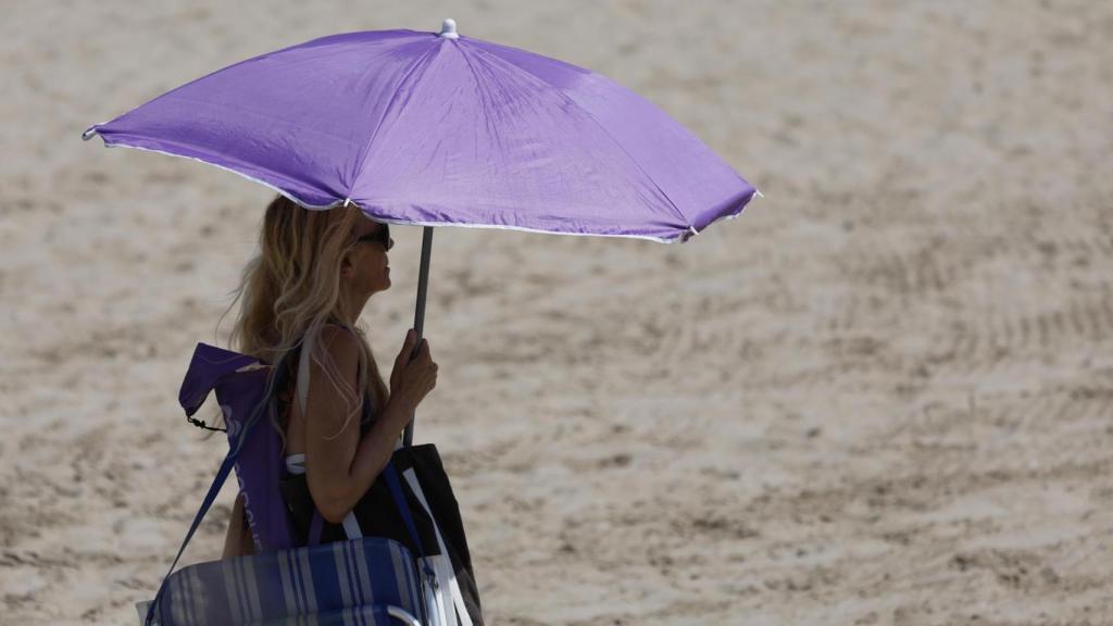 Una mujer protegiéndose del sol con un paraguas en una playa valenciana