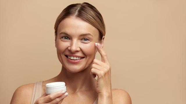 Mujer aplicándose crema en el contorno de ojos.