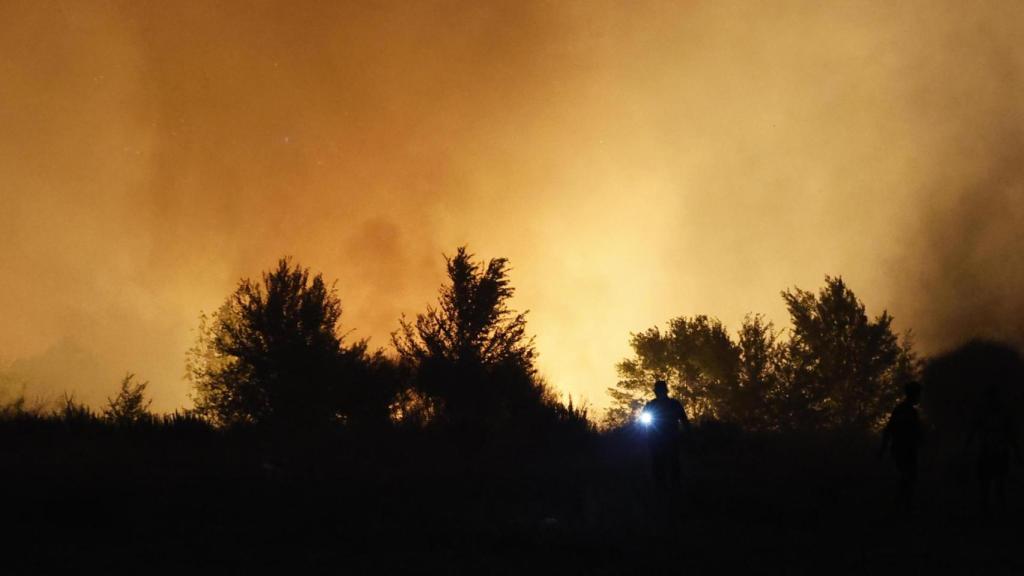 Un agente de Policía local evacúa a personas en el incendio que se ha declarado en la tarde de este lunes en la localidad madrileña de Tres Cantos