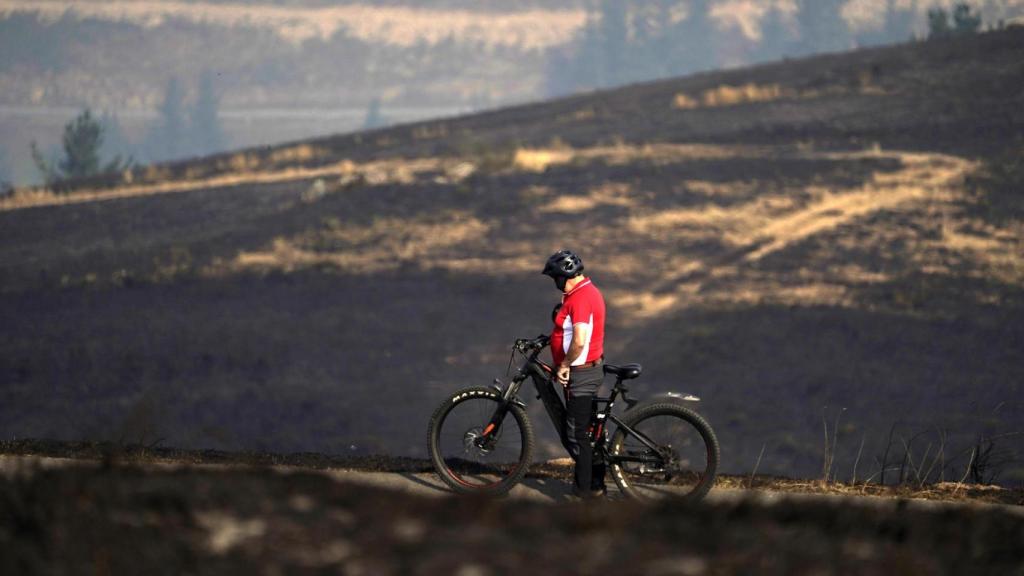 Una persona circula en bicicleta por la zona quemada en las proximidades del Santuario de la Virgen del Acebo, en Asturias.