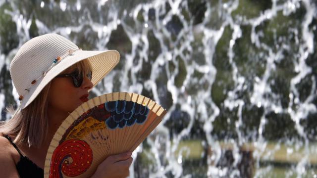 Una mujer se protege del sol con un sombrero y un abanico.