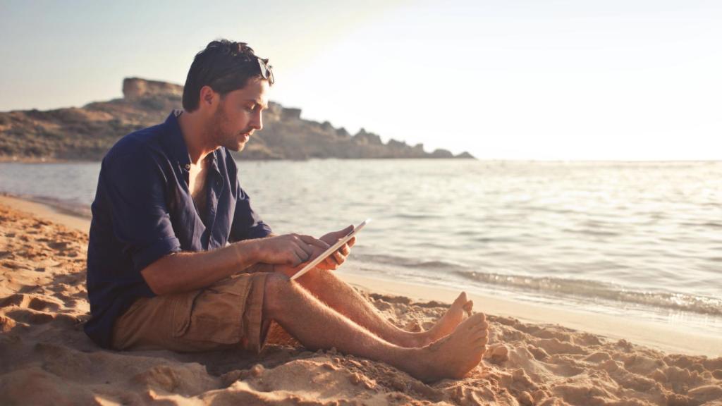 Un hombre leyendo un libro electrónico en la playa