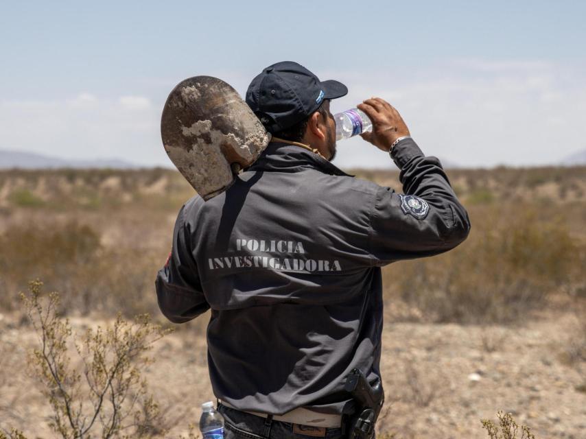 Bajo el intenso sol del desierto, un policía de investigación se prepara para continuar la búsqueda en el arroyo El Navajo, cargando con las herramientas necesarias para excavar en el terreno árido.