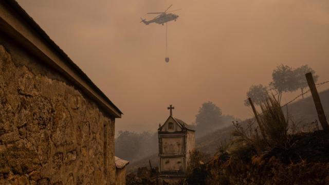Un helicóptero de control de incendios sobrevuela el cementerio la localidad de Vilar durante el incendio forestal que permanece activo en Chandrexa de Queixa (Ourense).