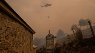 Un helicóptero de control de incendios sobrevuela el cementerio la localidad de Vilar durante el incendio forestal que permanece activo en Chandrexa de Queixa (Ourense).