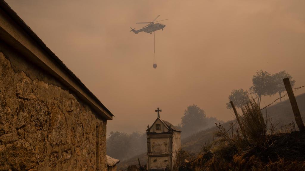 Un helicóptero de control de incendios sobrevuela el cementerio de Vilar durante un incendio forestal.