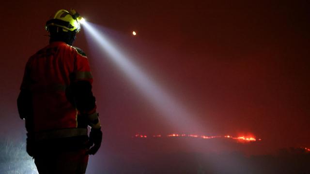 Un bombero utiliza una linterna mientras trabaja para extinguir un incendio forestal en As Fermosas, en Orense.